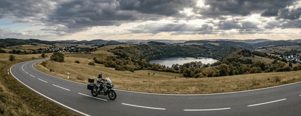 Motor op een open weg in de Vulkaaneifel met glooiende heuvels en een kratermeer op de achtergrond
